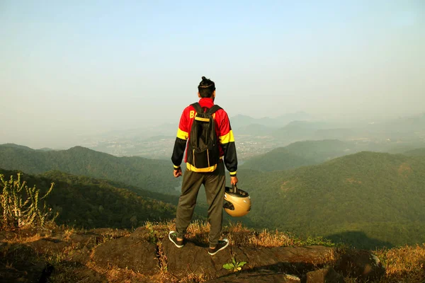 Jovem com mochila e capacete em pé no topo de uma montanha e desfrutando de vista para o vale — Fotografia de Stock