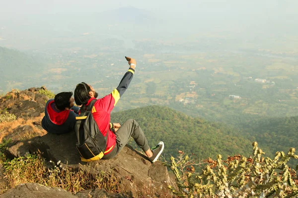 Dois meninos com mochila sentando-se no topo de uma montanha e desfrutando de vista para o vale — Fotografia de Stock