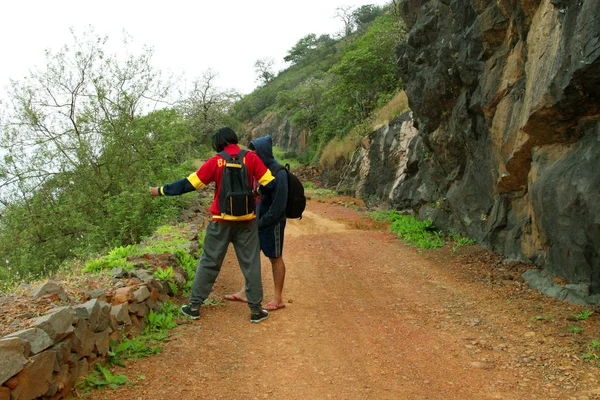 Bir dağın tepesinde oturan ve Vadi Manzaralı zevk alarak sırt çantası ile iki genç erkek — Stok fotoğraf