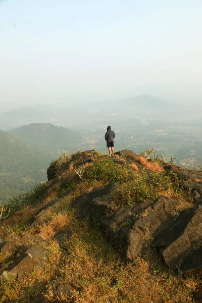 Jovem de pé no topo de uma montanha e desfrutando de vista para o vale — Fotografia de Stock