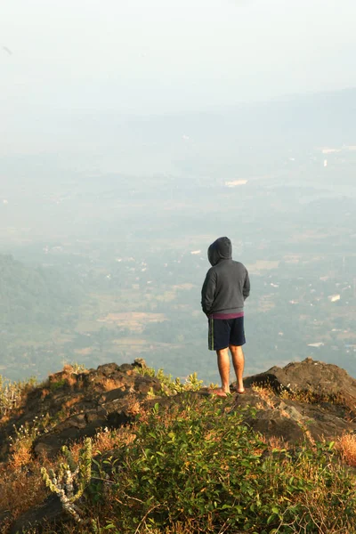 Jovem de pé no topo de uma montanha e desfrutando de vista para o vale — Fotografia de Stock