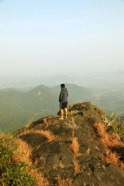 Jovem de pé no topo de uma montanha e desfrutando de vista para o vale — Fotografia de Stock