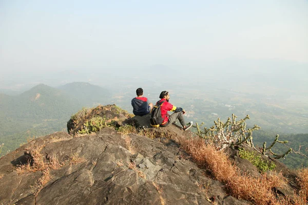 Bir dağın tepesinde oturan ve Vadi Manzaralı zevk alarak sırt çantası ile iki genç erkek