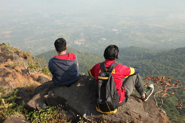 Dos chicos jóvenes con mochila tomando sentado en la cima de una montaña y disfrutando de la vista del valle — Foto de Stock
