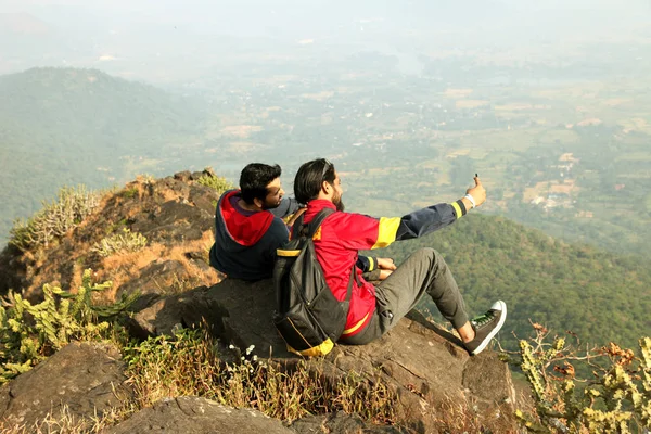 Two Young boys with backpack taking sitting on the top of a mountain and enjoying valley view — Stock Photo, Image