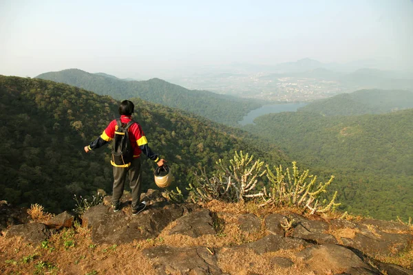 Jovem com mochila e capacete em pé no topo de uma montanha e desfrutando de vista para o vale — Fotografia de Stock