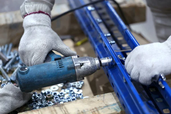 One warehouse worker in with power tool tightening screw during rack arrangement erection work