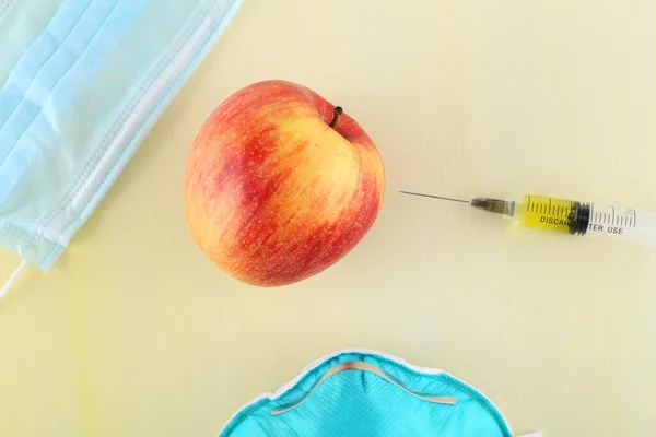 Chemical additives in food or genetically modified fruit concept.  Red apple with syringes of chemicals. Isolated on red background.