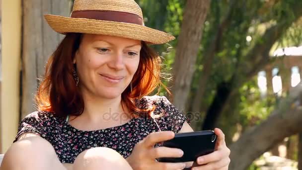 Mulher bonito relaxa no jardim desfrutando de seu smartphone ao sol — Vídeo de Stock