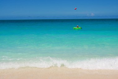 Pembe şapkalı bir kız Karayipler 'de bir hayat kurtarıcıda rahatlıyor ve bir paraşütçüyü izliyor.