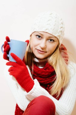 Kırmızı şapka ve Kupası: örme eldiven ve kap eğleniyor bir desen kar taneleri, beyaz kazak güzel kız portresi içki içecek mutlu gülümseyerek ve ışık kameraya bakarak kopyalama alanı arka plan
