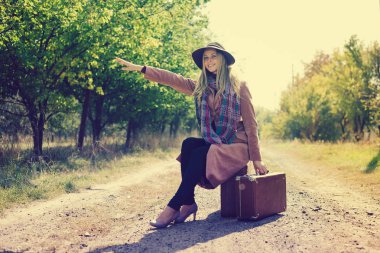 Klasik valizli bir kadın boş bir yolda otostop çekiyor. Yurt dışına seyahat