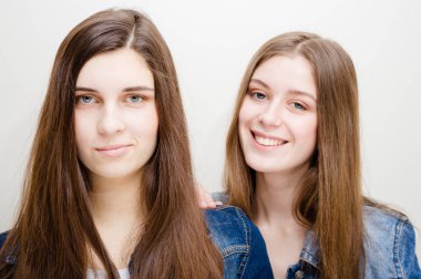 Uzun siyah saçlı ve doğal makyaj kameraya bakarak gülen mutlu kot gömlek giymiş olan iki güzel genç kadın portre portre