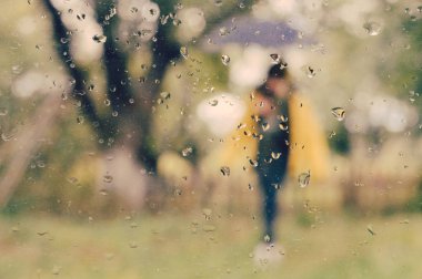 Blurred picture of woman standing under umbrella with raindrops on window glass foreground with copy space clipart