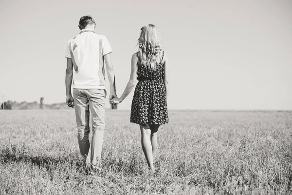 Pareja joven caminando en el campo con flores a la luz del sol en blanco y negro — Foto de Stock