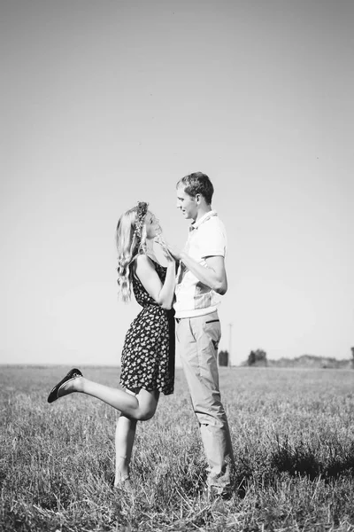 Jeune couple marchant dans le champ avec des fleurs au soleil en noir et blanc — Photo