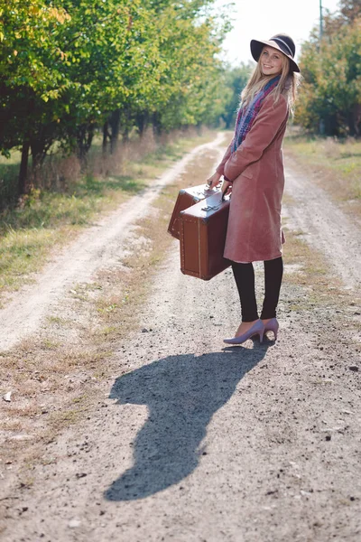 Mujer en sombrero y abrigo con maleta en la carretera — Foto de Stock