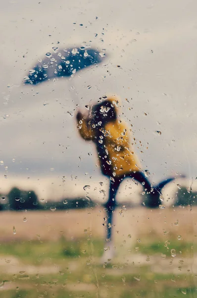 コピー スペースと灰色の空の下のウィンドウ ガラスの前景に雨と傘の下で立っている女性の画像をぼやけ — ストック写真