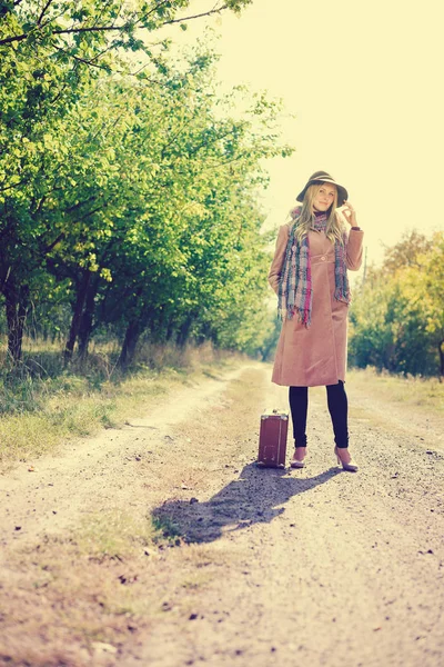 Portré nő kalap és kabát bőrönddel az úton háttér szabadban — Stock Fotó