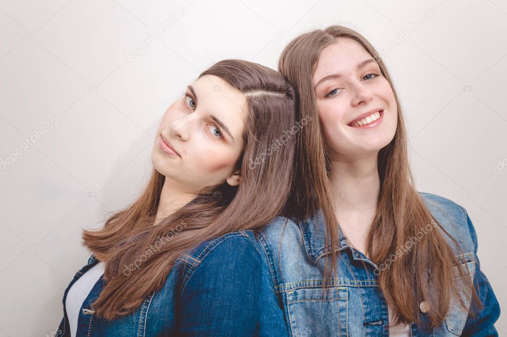 Closeup portrait of two beautiful young women with long dark hair and natural makeup wearing jeans shirts happy smiling looking at camera