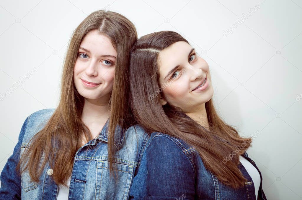 Closeup portrait of two beautiful young women with long dark hair and natural makeup wearing jeans shirts happy smiling looking at camera