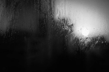 Bulanık, yoğunlaştırılmış yağmur damlalarına, parlayan gökyüzüne ve pencereli binalara yakın çekim