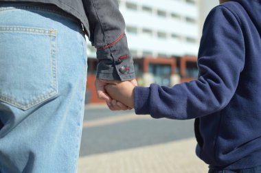Anne sokakta yürürken oğlunun elini tutuyor.
