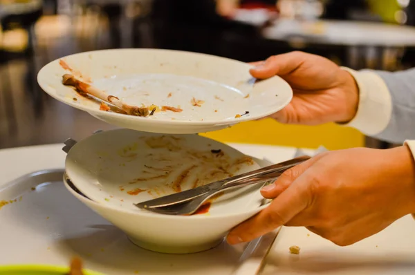 Cerca de la mano de un hombre que lleva platos sucios y vajilla en el fondo de la mesa de la cena terminada. Comer hecho tiempo limpio, ventana abstracta bokeh espacio —  Fotos de Stock
