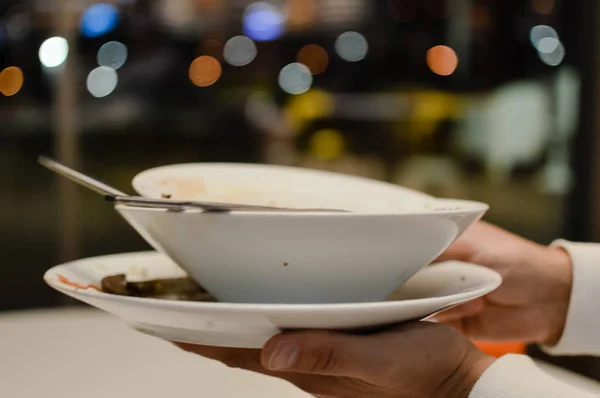 Cerca de la mano de un hombre que lleva platos sucios y vajilla en el fondo de la mesa de la cena terminada. Comer hecho tiempo limpio, ventana abstracta bokeh espacio —  Fotos de Stock