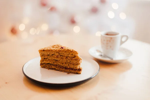 İtalyan kahve fincanı ve ballı kek Noel ağacının yanındaki masada beyaz bokeh ile. — Stok fotoğraf