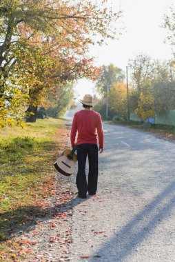 Yalnız gitarist sonbaharda boş köy yoluna bakıyor.