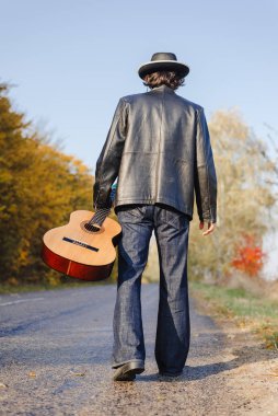 Yalnız gitarist sonbaharda boş köy yoluna bakıyor.