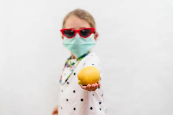 金发小女孩戴着一次性口罩 戴着太阳镜 白色背景上戴着黄色柠檬维生素C — 图库照片