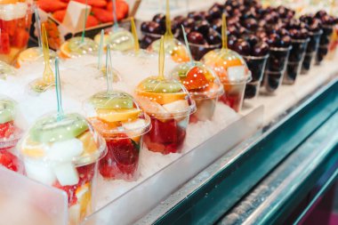 Meyve salatası plastik bardaklarda, içinde çatal ve atıştırmalık bir şeyler olan bir marketin tezgahında.