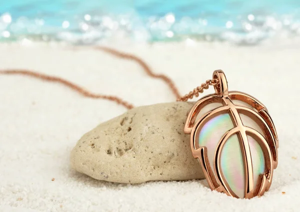 Colgante de joyas doradas en la playa de arena de verano con fondo de mar —  Fotos de Stock