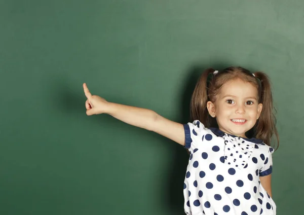 Sorrindo criança menina mostrar com um dedo em branco escola quadro negro, c — Fotografia de Stock