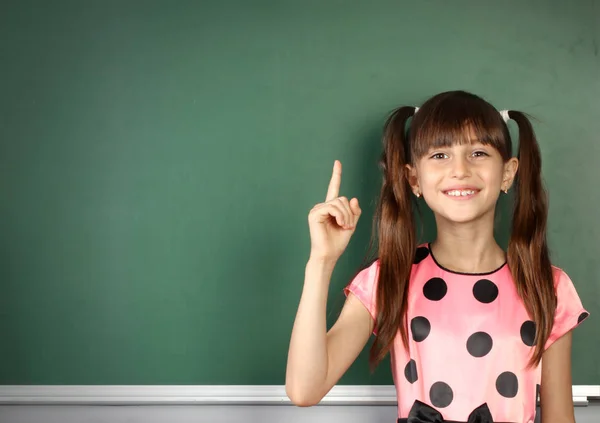 Smiling child girl show with a finger empty school blackboard, c — Stock Photo, Image