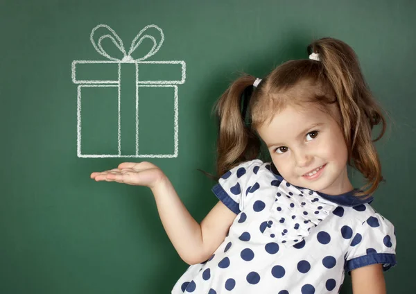 Souriant enfant fille tenir tiré boîte cadeau près du tableau noir de l'école — Photo