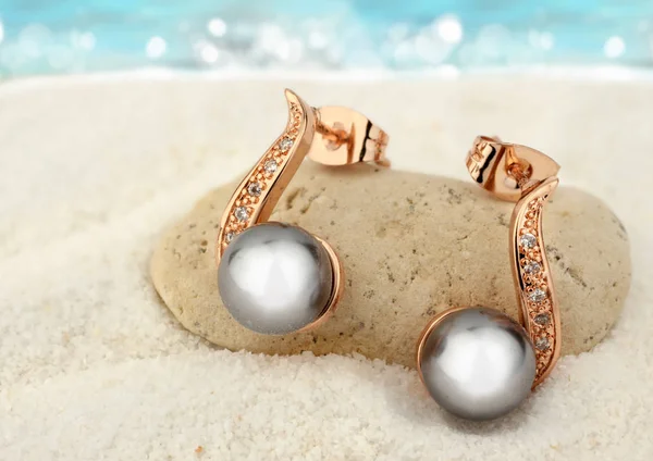 Šperky náušnice s černými perlami na pískové pláži pozadí — Stock fotografie