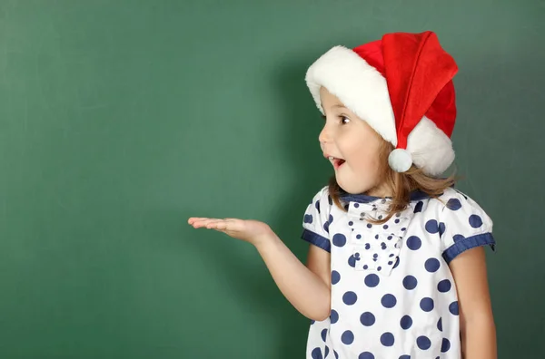 Überrascht Kind Mädchen mit Weihnachtsmütze hält seine Hand in der Nähe von leeren sc — Stockfoto