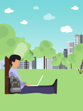 Genç adam çimenlerde oturuyor ve çalışıyor. Freelanser şehir parkında çalışıyor. Ağacın altında dizüstü bilgisayarı olan iş adamı programcı.