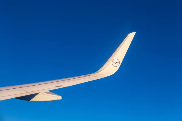 Asa de aeronaves com logotipo lufthansa voando no céu por do sol — Fotografia de Stock