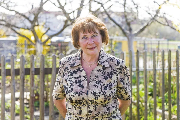 Mulher idosa feliz está de pé orgulhoso em seu jardim e sorri — Fotografia de Stock