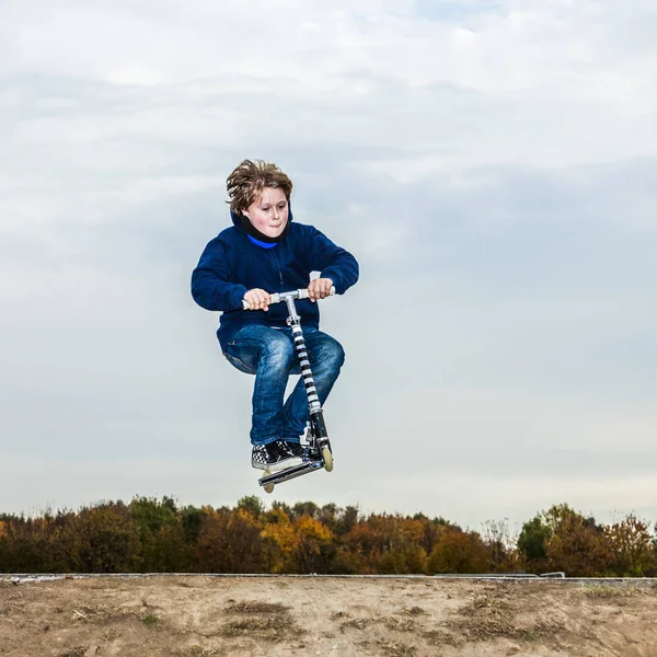 Chico disfruta saltando con su scooter sobre una rampa — Foto de Stock