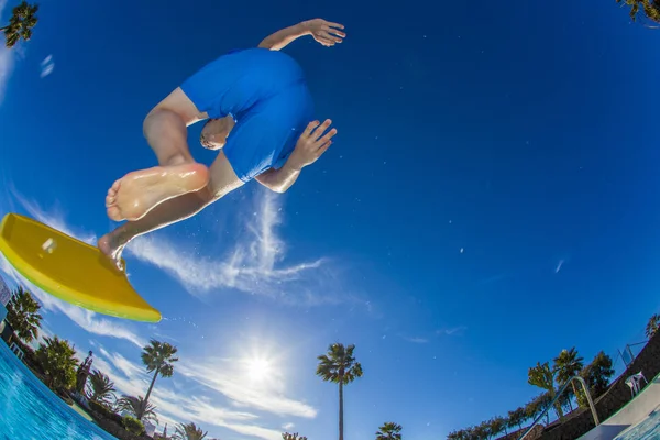Garçon s'amuse à sauter avec la planche de surf dans la piscine — Photo