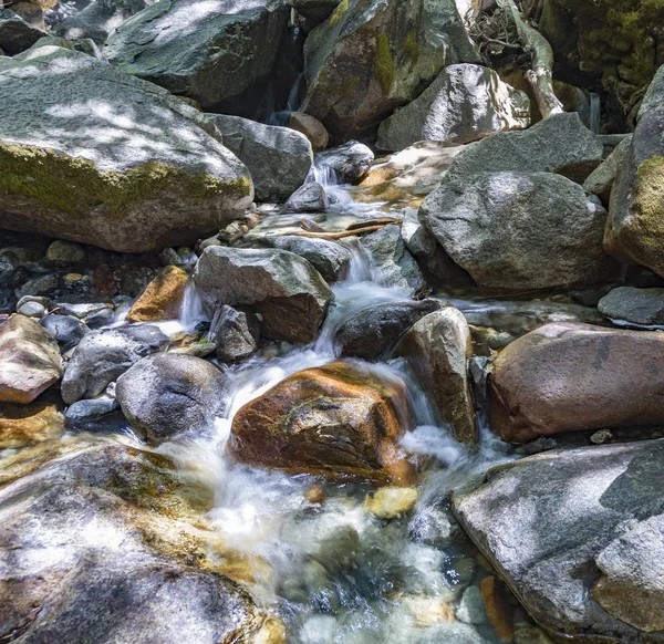 Pedras coloridas na água fria clara de um riacho — Fotografia de Stock