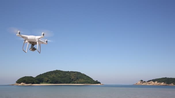 Hvit fjernstyrt drone som flyr i luft med kyst og blå himmel – stockvideo