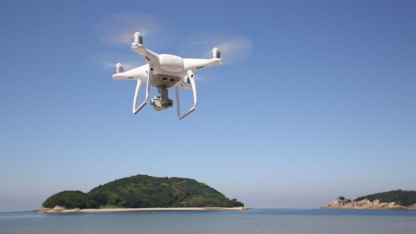 White remote controlled drone flying in air with shore and blue sky — Stock Video