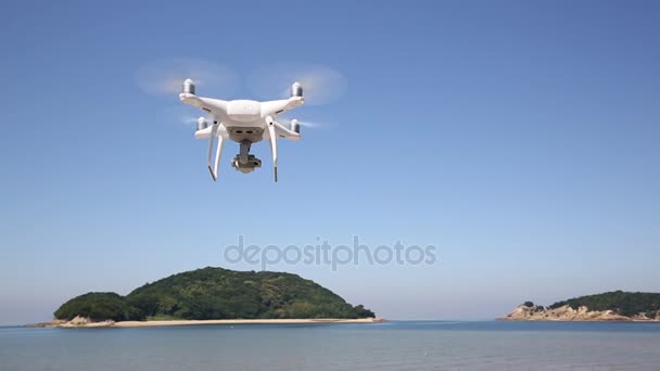 Hvit fjernstyrt drone som flyr i luft med kyst og blå himmel – stockvideo