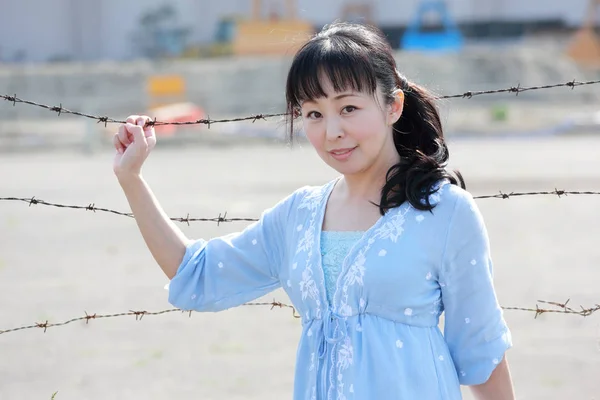Mladá asijská žena stojí na barbwire plot — Stock fotografie